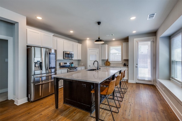 kitchen with white cabinets, a sink, stainless steel appliances, a kitchen bar, and visible vents