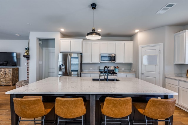 kitchen featuring visible vents, a center island with sink, wood finished floors, a sink, and stainless steel appliances