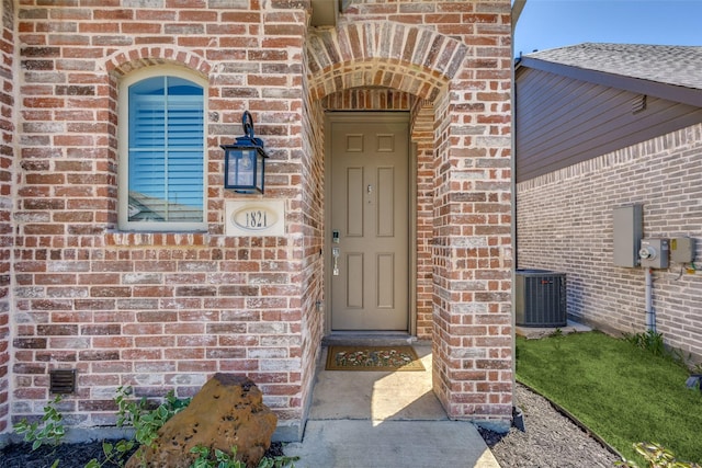 view of exterior entry with brick siding and central AC