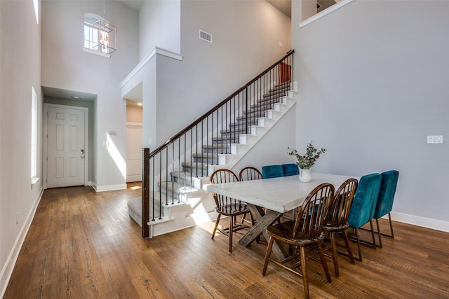 dining space with baseboards, wood finished floors, a towering ceiling, visible vents, and stairway