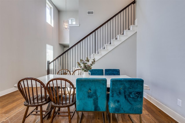 dining area with a high ceiling, stairs, baseboards, wood finished floors, and visible vents