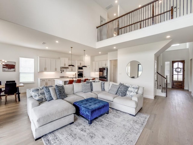 living room featuring light wood-type flooring, a high ceiling, visible vents, and stairway