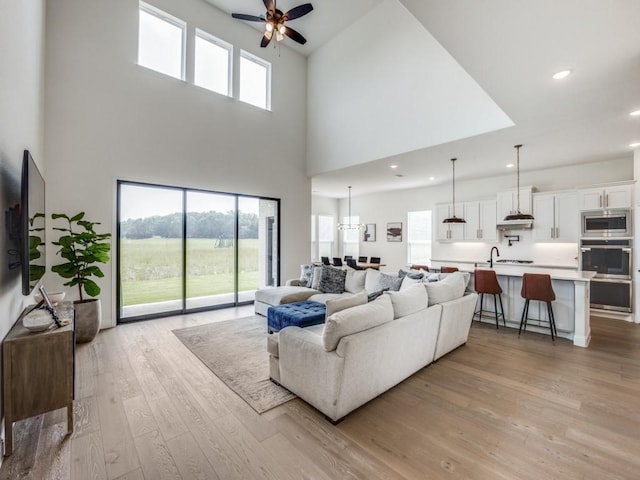 living area featuring recessed lighting, ceiling fan, a high ceiling, and light wood-style floors