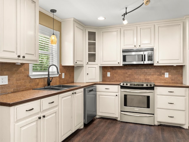 kitchen featuring hanging light fixtures, appliances with stainless steel finishes, a sink, decorative backsplash, and dark wood-style floors