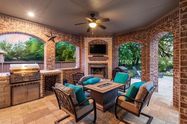 view of patio / terrace with grilling area, ceiling fan, fence, an outdoor brick fireplace, and an outdoor kitchen