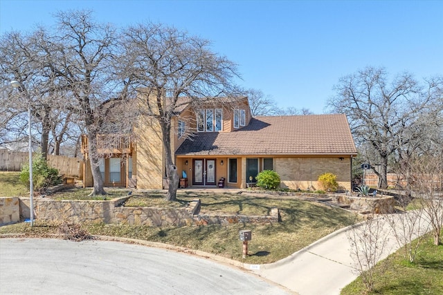view of front of property featuring fence, a front lawn, brick siding, french doors, and a tiled roof
