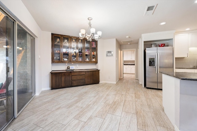kitchen featuring visible vents, an inviting chandelier, glass insert cabinets, stainless steel refrigerator with ice dispenser, and dark stone countertops