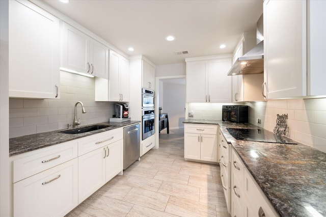 kitchen featuring wall chimney range hood, visible vents, appliances with stainless steel finishes, a sink, and white cabinets