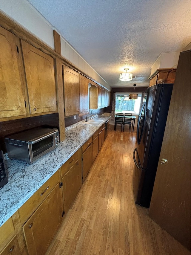 1207 W Cage St, Stephenville, TX 76401 - kitchen featuring brown cabinetry, freestanding refrigerator, light wood-type flooring, a textured ceiling, and a sink