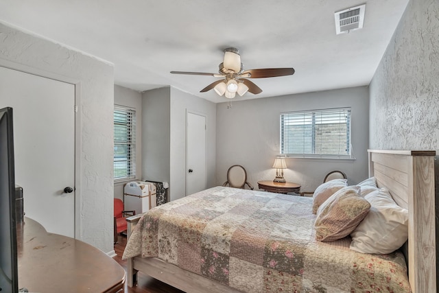 bedroom with a ceiling fan, a textured wall, visible vents, and wood finished floors