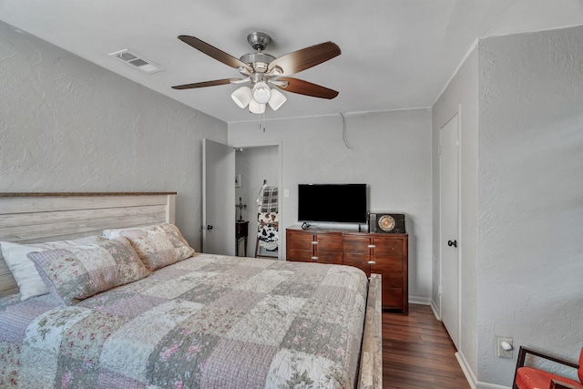 bedroom with visible vents, a textured wall, baseboards, dark wood-type flooring, and a ceiling fan