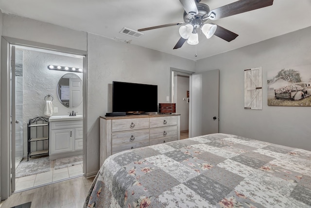 bedroom with visible vents, a ceiling fan, a sink, light wood finished floors, and ensuite bath