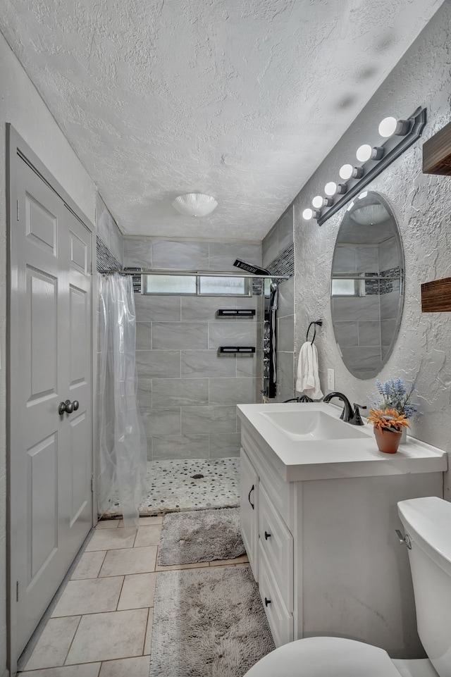 bathroom with vanity, toilet, a textured ceiling, tile patterned floors, and a tile shower
