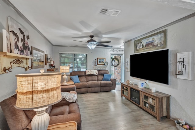 living room featuring visible vents, ornamental molding, a textured wall, wood finished floors, and ceiling fan