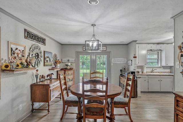 dining space with a textured ceiling, an inviting chandelier, ornamental molding, and light wood-style floors