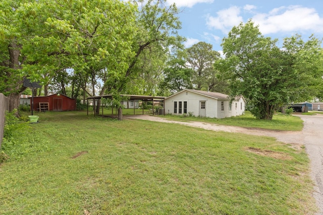 view of yard with dirt driveway, fence, an outbuilding, and a carport