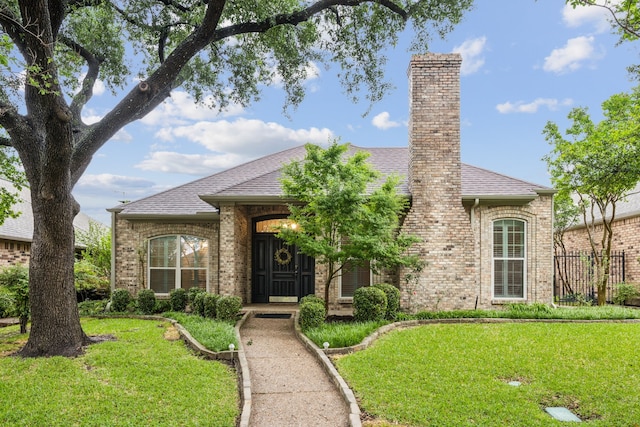 view of front of house featuring brick siding, fence, a shingled roof, and a front yard