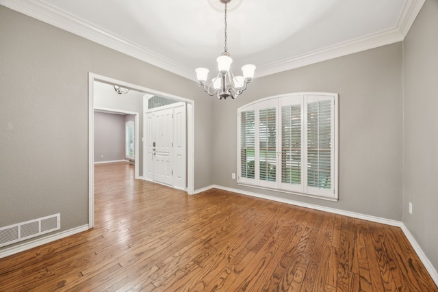 unfurnished dining area with an inviting chandelier, crown molding, wood finished floors, and visible vents