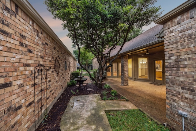 view of side of home featuring a ceiling fan, a patio, a shingled roof, and brick siding