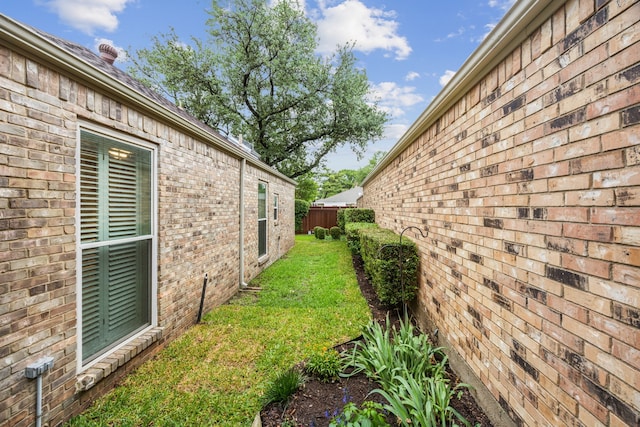 view of property exterior with a lawn, brick siding, and fence
