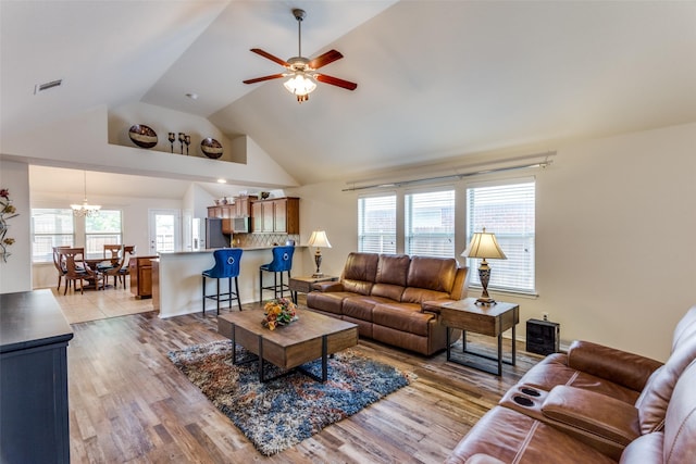 living area featuring light wood-type flooring, ceiling fan with notable chandelier, lofted ceiling, and visible vents