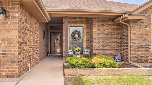 entrance to property featuring a porch, brick siding, and roof with shingles