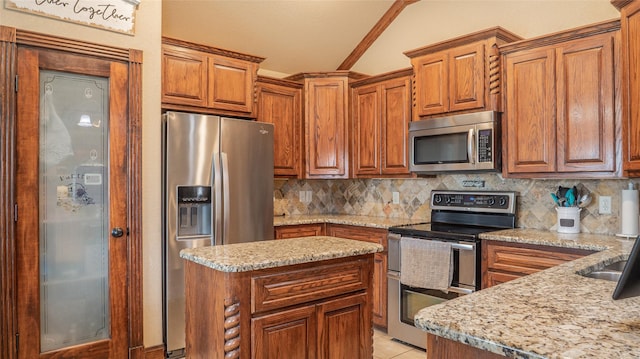 kitchen featuring brown cabinetry, appliances with stainless steel finishes, backsplash, and vaulted ceiling