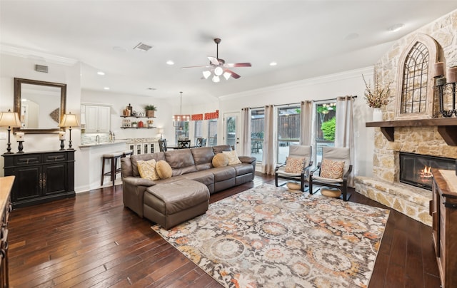 living room with ceiling fan, visible vents, crown molding, a fireplace, and dark wood-type flooring