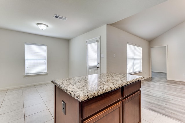 kitchen featuring visible vents, baseboards, a center island, light stone counters, and light tile patterned floors