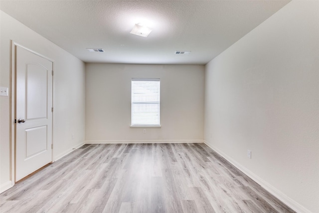 spare room featuring visible vents, a textured ceiling, light wood finished floors, and baseboards