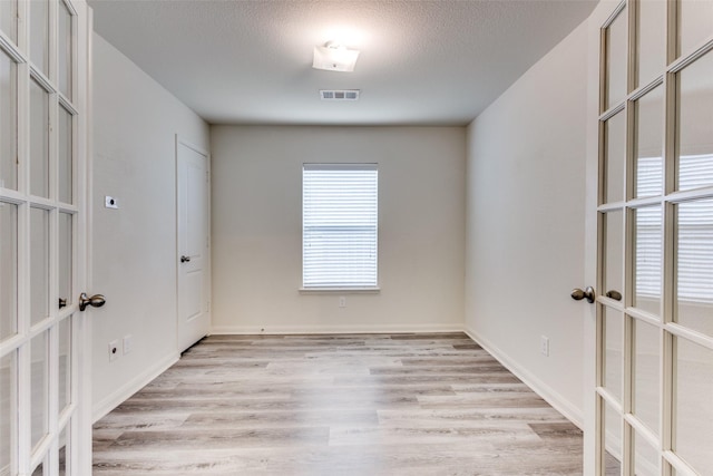empty room featuring a textured ceiling, french doors, light wood-style flooring, and visible vents