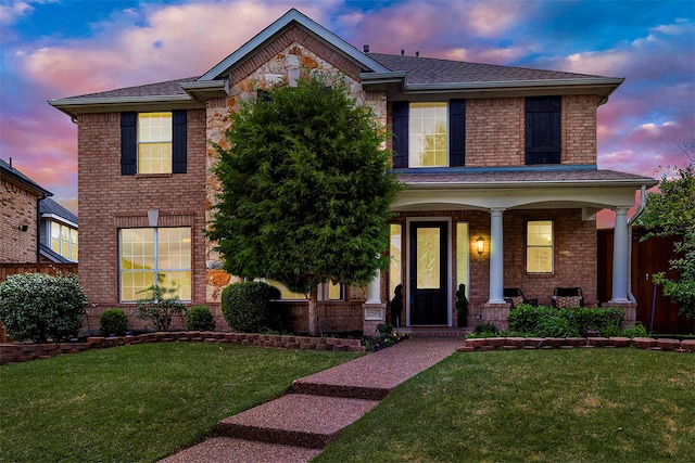 traditional-style home featuring roof with shingles, covered porch, a yard, and brick siding