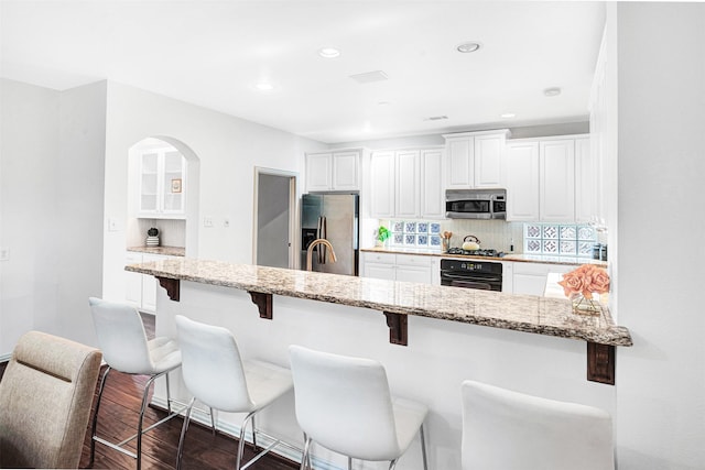 2283 Fox Crossing Ln, Frisco, TX 75036 - kitchen with a breakfast bar area, backsplash, appliances with stainless steel finishes, light stone countertops, and white cabinetry