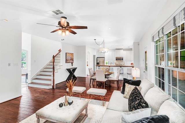 living area with visible vents, stairs, baseboards, ceiling fan, and dark wood finished floors