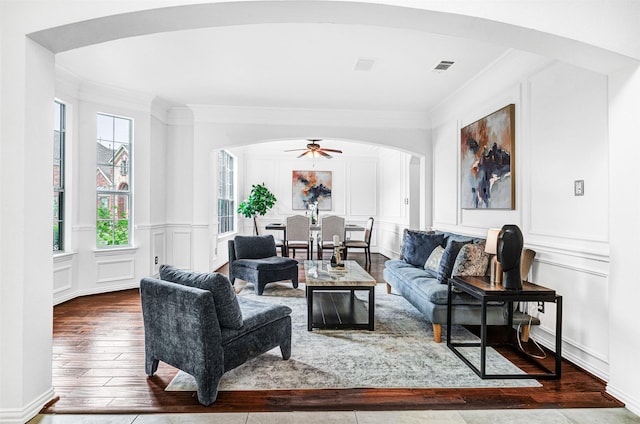 living area featuring arched walkways, ornamental molding, wood-type flooring, and a decorative wall