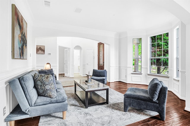 living area with arched walkways, ornamental molding, a decorative wall, and visible vents