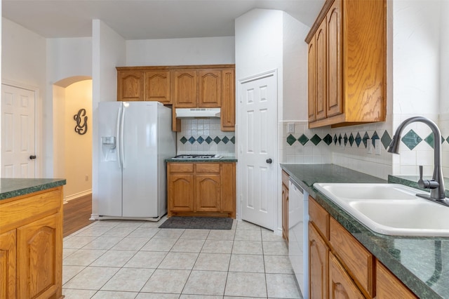 kitchen with white appliances, arched walkways, under cabinet range hood, a sink, and backsplash