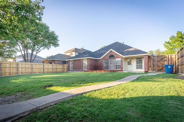 rear view of property with brick siding, a fenced backyard, a lawn, and a shingled roof
