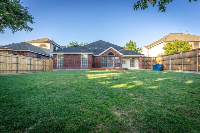 back of house featuring a fenced backyard, a yard, and brick siding