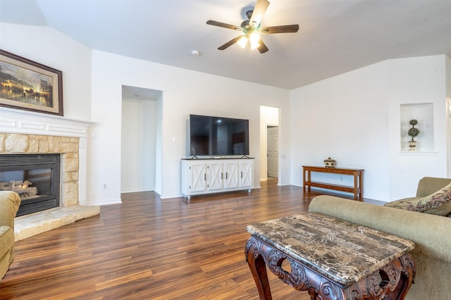 living area with baseboards, ceiling fan, a stone fireplace, and wood finished floors