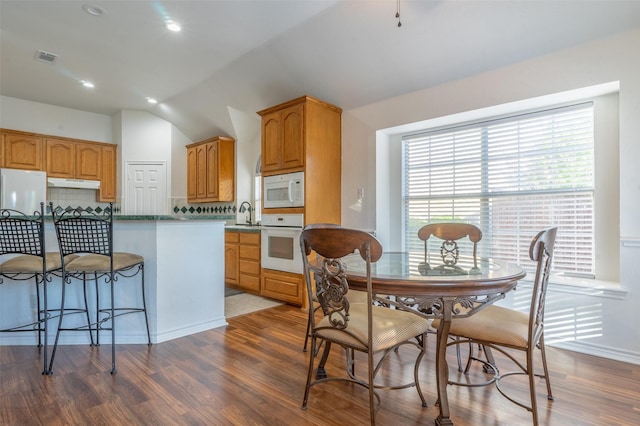kitchen featuring tasteful backsplash, wood finished floors, lofted ceiling, under cabinet range hood, and white appliances