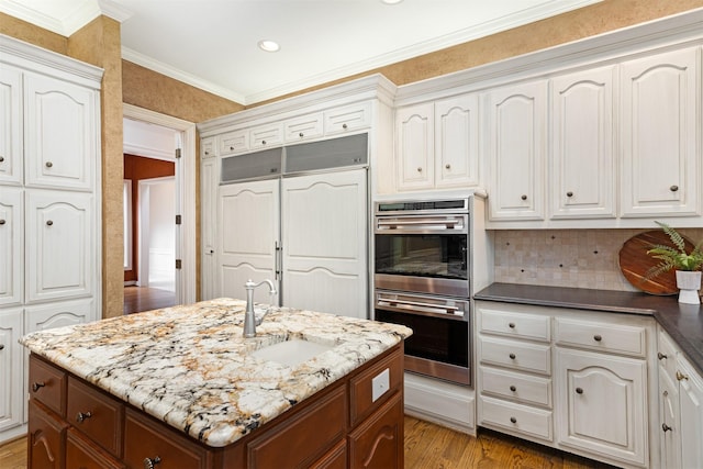 kitchen with double oven, paneled built in refrigerator, white cabinets, a sink, and backsplash