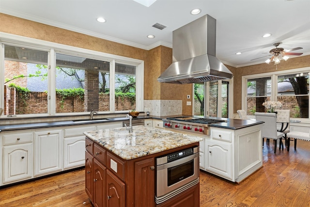 kitchen with island exhaust hood, a sink, plenty of natural light, and stainless steel gas cooktop