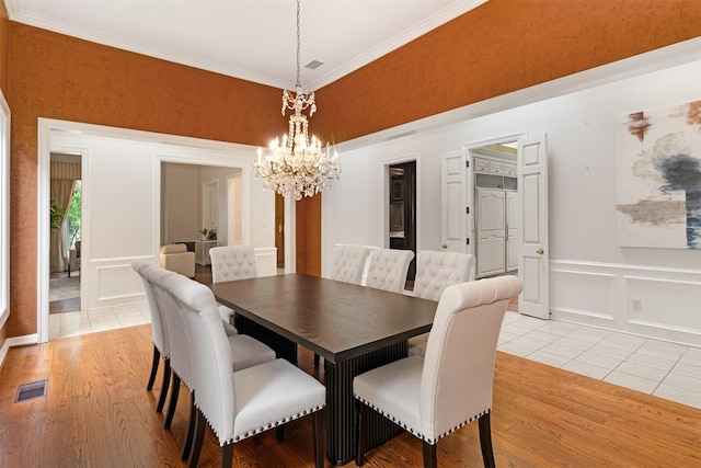 dining room featuring visible vents, crown molding, a chandelier, a decorative wall, and light wood-style flooring