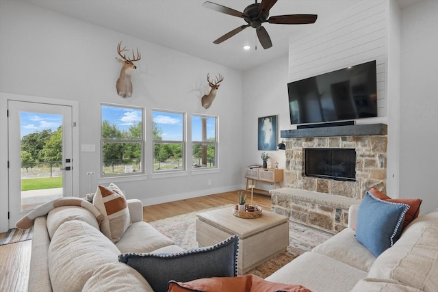living area with a ceiling fan, plenty of natural light, wood finished floors, and a towering ceiling