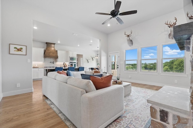 living room with a ceiling fan, baseboards, recessed lighting, and light wood finished floors