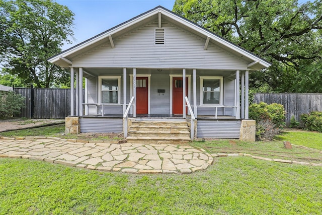 bungalow-style home with fence, covered porch, and a front yard