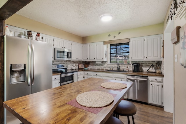 kitchen with decorative backsplash, wooden counters, a textured ceiling, appliances with stainless steel finishes, and a sink