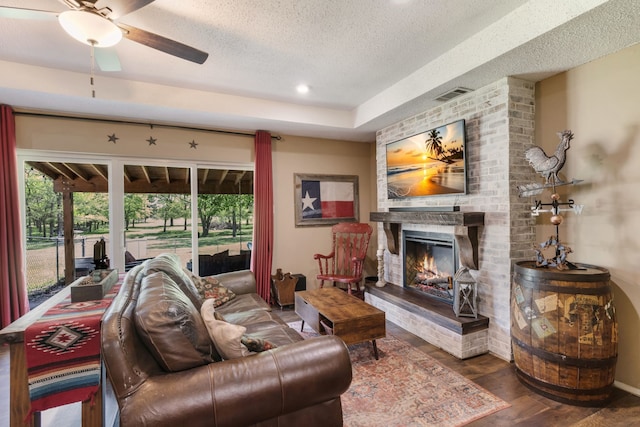 living area with ceiling fan, a fireplace, a textured ceiling, wood finished floors, and visible vents
