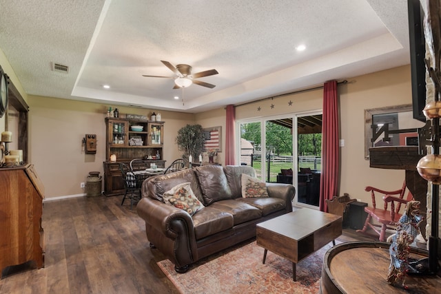 living room with ceiling fan, a textured ceiling, visible vents, wood-type flooring, and a tray ceiling